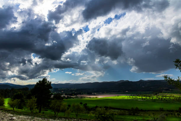istock Green meadow in a day with white and gray clouds and sun rays. 1371573854