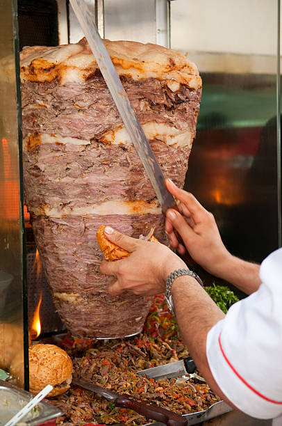 A man in the Middle East slices meat for a shawarma sandwich. Focus is centered on the bread in hand.
