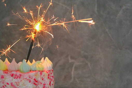 close-up on a dark background a cake with a lit sparkler. Concept - holiday, celebration, birthday. Horizontal photo, copy space