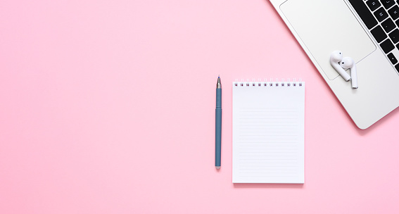 A white notebook next to a silver laptop on the left side of the frame against a pink background. Flat lay, copy space.