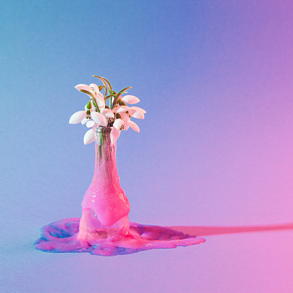 Bouquet of Snowdrops in an alien-like pink slime melting vase. Square metaverse composition with neon blue and purple lights.