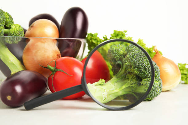 Different fresh vegetables and magnifying glass on table, closeup. Poison detection