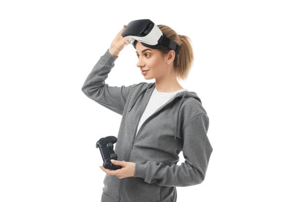 istock Young woman with VR goggles and gamepad standing against white background 1371620675