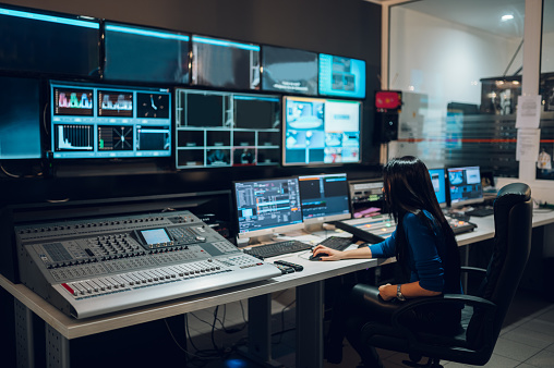 Middle aged beautiful woman working in a broadcast control room on a tv station. Entertainment news with footage equipment concept.
