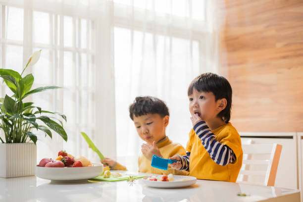 братья делают фруктовый салат, младший брат ест. - fruit salad fruit healthy eating making стоковые фото и изображения