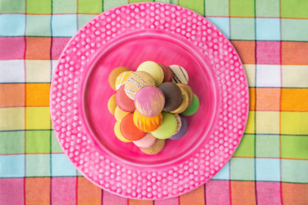 Macarons tower on pink dessert plate top view. Retro pink vintage tablecloth Easter table home kitchen. Assortment of pastel color macaron of different flavors. French pastry macaroons presentation.