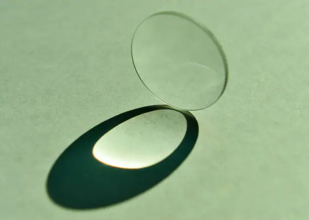 Close up image of daylight shine through clear circular convex lens with refection and refraction of light and cast artistic oval shape of shadow.