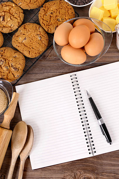 Freshly made chocolate chip cookies on a dark wood table with ingredients and spiral notebook.  For my complete baking series please click here: BAKING COLLECTION.   Alternative version of this file shown below: