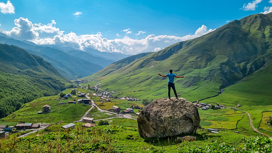 A man standing on a rock with an aerial view on the village Ushguli, near the Shkhara Glacier in the Greater Caucasus Mountains in Georgia, Svaneti Region.Chubedishi viewpoint.Patara Enguri River.Free