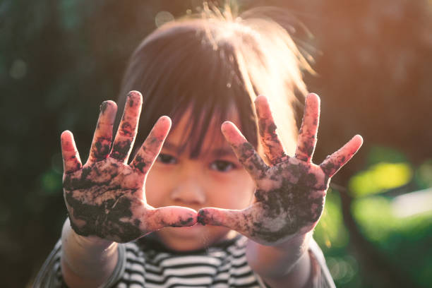 la bambina carina sorride e mostra le sue mani fangose mentre pianta alberi nel cortile. concetto educativo al di fuori della recinzione scolastica. - school farm foto e immagini stock