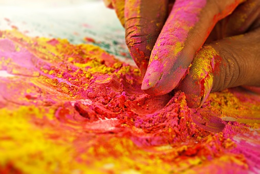 Colourful mix of holi powder colors in bright vibrant yellow and magenta pink splattered or spilled over white backgrounds being picked by a human hand. Ideal for posters, greeting cards, postcards related to the Indian Hindu festival of colors - Holi.