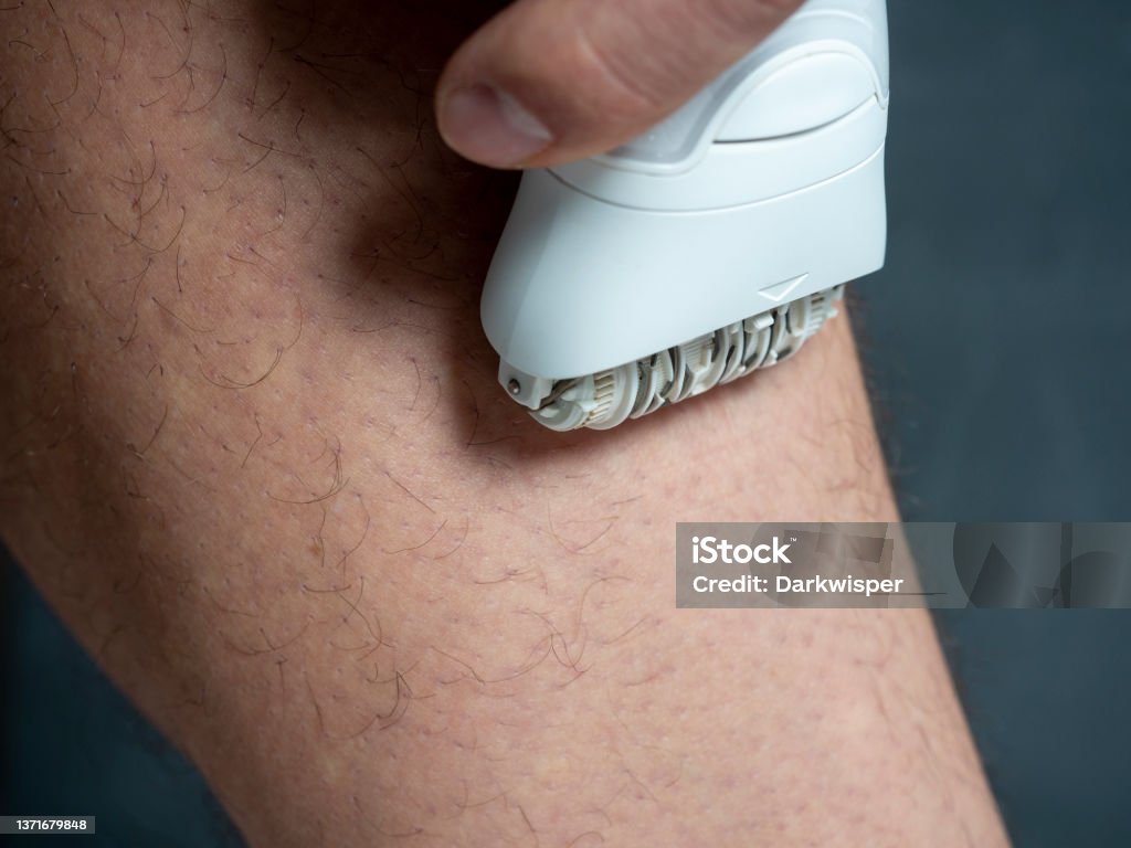 a man shaves his leg hair with a white electric depilator. Men's beauty. Close up Epilator Stock Photo