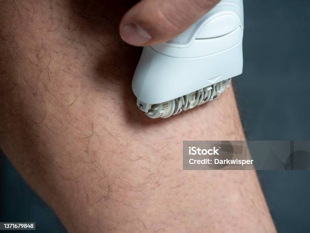 A Man Shaves His Leg Hair With A White Electric Depilator Mens Beauty Close Up Stock Photo - Download Image Now