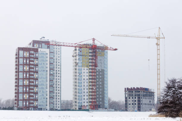 High-rise buildings under construction with red and yellow building cranes under falling snow in winter day