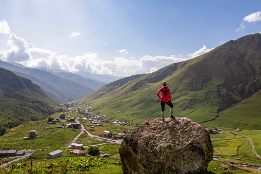 A woman standing on a rock with an aerial view on the village Ushguli, near the Shkhara Glacier in the Greater Caucasus Mountains in Georgia, Svaneti Region.Chubedishi viewpoint.Patara Enguri River