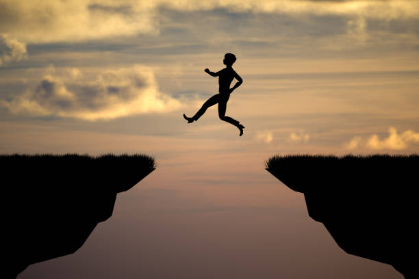 Silhouette woman jumping on a cliff with sunset sky background.