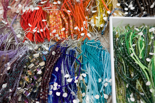 A variety of beads, baubles and stones on string, in piles of bins for jewelers and craft makers to purchase for making necklaces, earrings and other jewelry as hobbies.