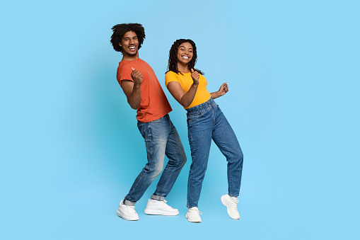 Positive african american young couple in casual summer outfits posing together on blue studio background, dancing and smiling at camera, panorama with copy space, full length shot