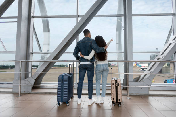 voyage aérien. couple romantique regardant la fenêtre de l’aéroport et pointant vers l’extérieur - bâtiment vu de lextérieur photos et images de collection