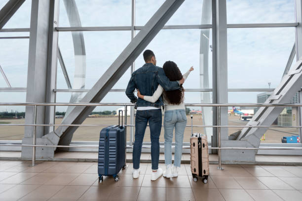 воздушное путешествие. романтическая пара смотрит в окно в аэропорту и указывает в сторону - hug point стоковые фото и изображения