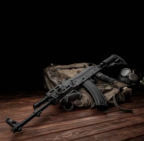 Photo of Soviet carbine in modern body kit. Weapons of Russia and the Soviet Union. Classic Soviet AK assault rifle and gas mask on a wooden background.