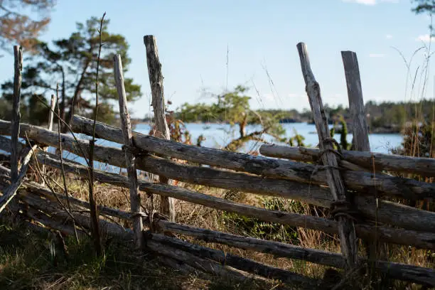 Traditional old wooden roundpole fence on the countryside. Idyllic view of the countryside and landscape with the water and forest in the background. Photo taken in Oskarshamn, Sweden.