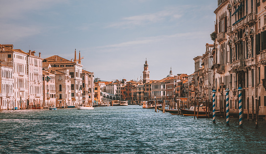 Beautiful vintage landscape city view of famous Canal Grande with tourist people on old boats, gondolas and canoes moving on the river on a sunny day with blue sky in summer, Venice, Veneto, Italia.