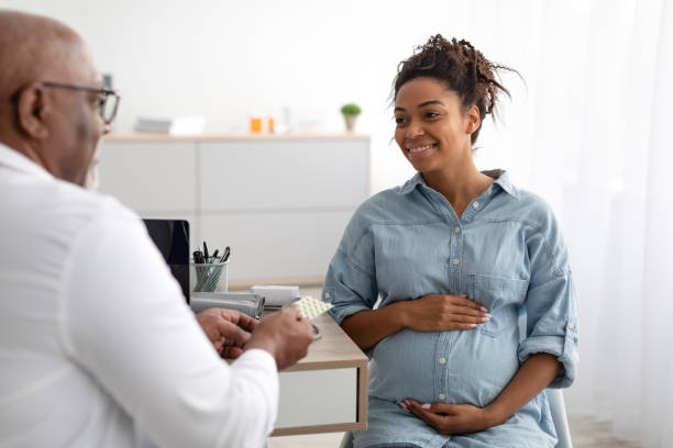 reifer erfahrener schwarzer arzt zeigt schwangeren frauen pillen - schwanger stock-fotos und bilder