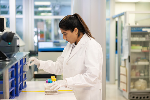 Side view of a woman medical researcher working in the science lab. Female scientist wearing lab coat working with samples in modern laboratory.