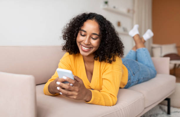 istock Millennial black lady using cellphone, lying on couch at home, working or studying remotely 1371703501