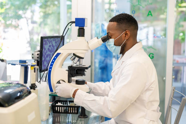 Side view of a medical researcher looking through a microscope Side view of a medical researcher looking through a microscope. Male doctor wearing protective face mask using an electron microscope in a medical research center. biochemistry stock pictures, royalty-free photos & images