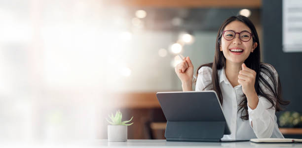 elegante geschäftsfrau sitzt im büro mit digitalem tablet. aufgeregte asiatische geschäftsfrau, die die hände hebt, um zu gratulieren, während sie am laptop im büro arbeitet. - thai culture fotos stock-fotos und bilder