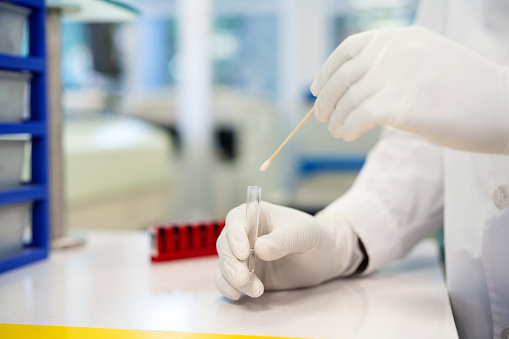 Close-up of a researcher using a cotton swab and test tube in a laboratory. Cropped shot of unrecognizable medial scientist hands wearing protective glove working in a research lab.