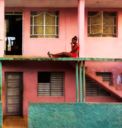 Varadero, Cuba - August 07, 2016:  Sad local young woman in red, seating outside on the floor of her almost finished house.