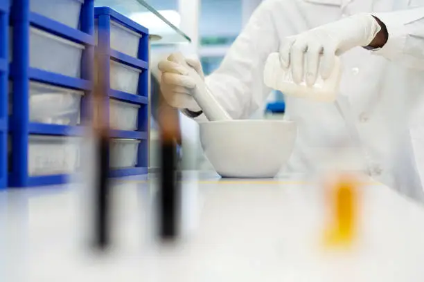 Midsection of a scientist making medicine in laboratory. Professional using mortar and pestle pouring solution from bottle.