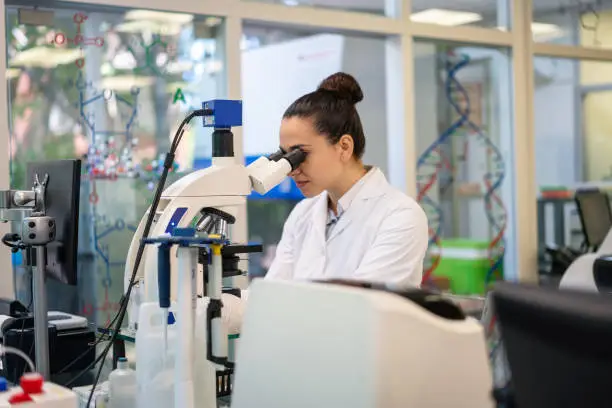 Scientist in lab doing research using microscope. Female scientist looking through microscope in science laboratory.