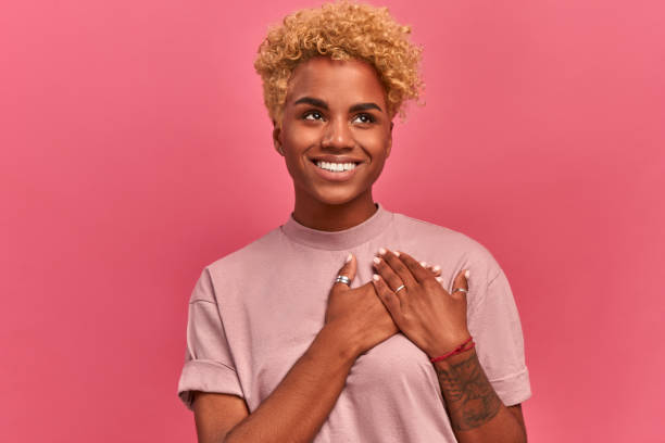 istock Smiling cheerful dark skinned young female keeps palms on heart, expresses appreciation, pleasure and gratitude, depicts symbol of fight against breast cancer on pink wall. 1371708030