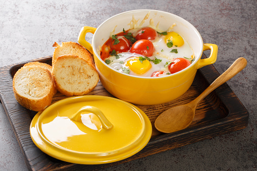 Eggs en Cocotte baked with tomato, parsley, meat, cheese closeup in the wooden tray on the table. Horizontal