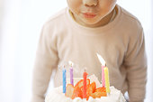 彼の誕生日ケーキにろうそくを吹き消すアジアの少年