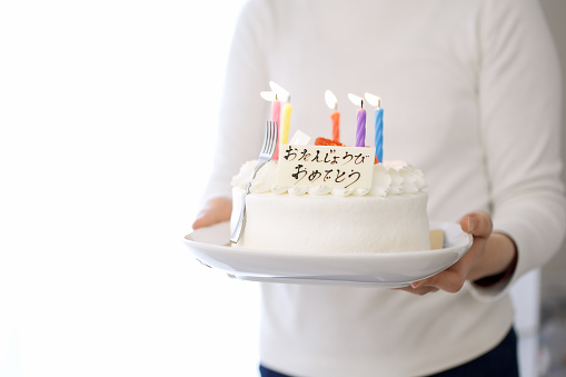 Asian mom carrying a cake that says Happy Birthday in Japanese