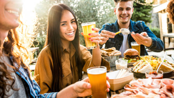 amici multietnici felici che cenano insieme al ristorante del pub del birrificio - giovani che fanno festa estiva in giardino mangiando cibo e bevendo birra - focus sulle donne asiatiche - dining burger outdoors restaurant foto e immagini stock