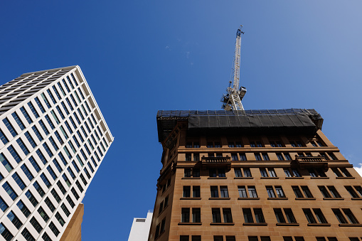 Low angle view of old and new tall buildings. A crane is on top of the older building.