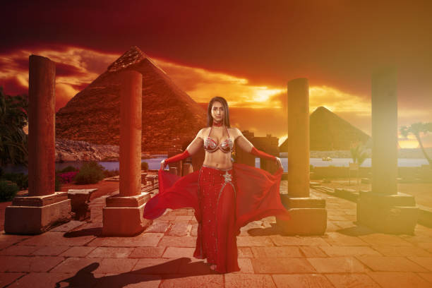 Oriental dancer in red costume at sunset dancing in a temple ruins with pyramids in the background