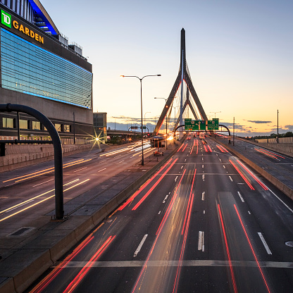 Boston, MA, USA - July 20, 2018: view of the architecture of Boston in Massachusetts, USA at sunset with the iconic Zakim Bridge and highway 93 North and lots of cars passing by leaving a light trail.