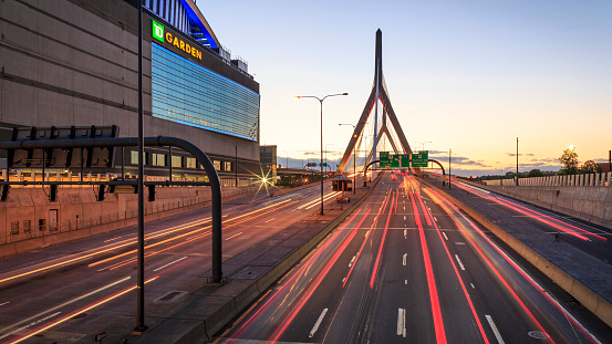 Boston, MA, USA - July 20, 2018: view of the architecture of Boston in Massachusetts, USA at sunset with the iconic Zakim Bridge and highway 93 North and lots of cars passing by leaving a light trail.