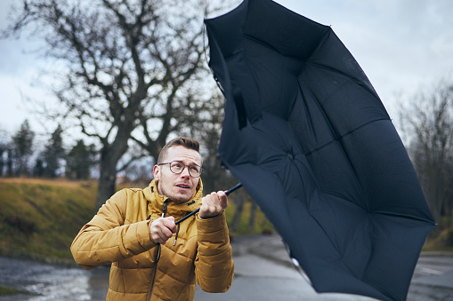Man holding broken umbrella in strong wind during gloomy rainy day. Themes weather and meteorogy. 