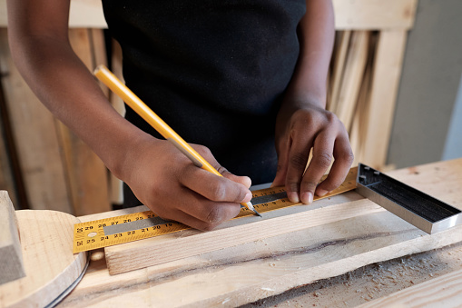 Close up of African-American boy measuring piece of wood in carpentry workshop, copy space