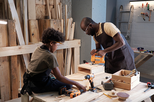 Portrait of father and son building wooden birdhouse together and bonding in workshop
