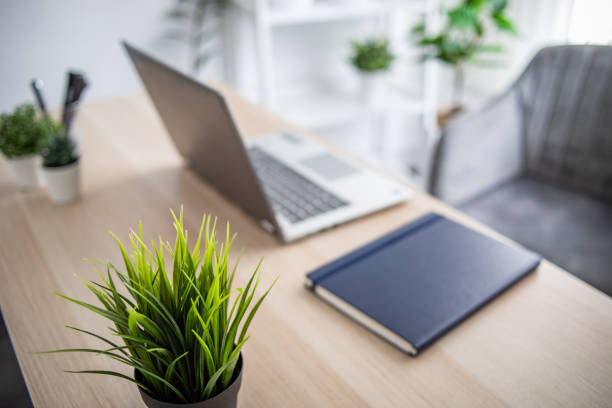 Laptop Computer on a Modern Wooden Business Desk with a Notepad and Pen in Unfocused Background