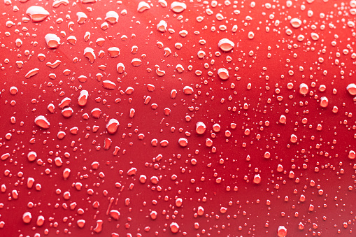 Small raindrops collect on the surface of a shiny metal car door.